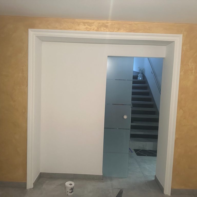 Weiße Tür mit Glaselementen, dahinter eine Treppe, goldene Wandfarbe.